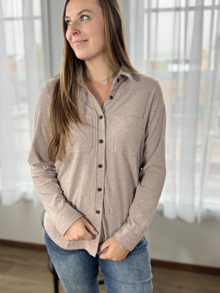 Woman wearing a beige button-up shirt and jeans indoors with blurred background
