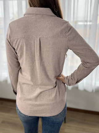 Person wearing a beige long-sleeve shirt with a blurred background