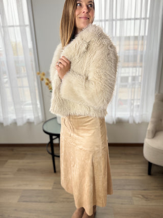 Woman wearing a cream fur coat and beige dress indoors.