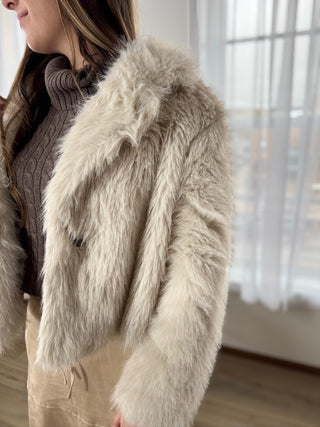 Person wearing a fluffy white jacket indoors with a blurred background