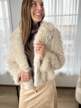 Woman wearing a beige fur coat indoors with a blurred background