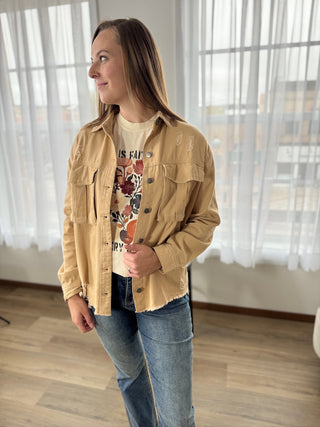Woman wearing a beige jacket over a graphic t-shirt and jeans indoors.