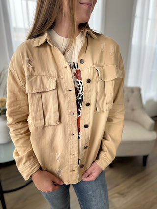 Person wearing a beige jacket in a room with light-colored walls and furniture.