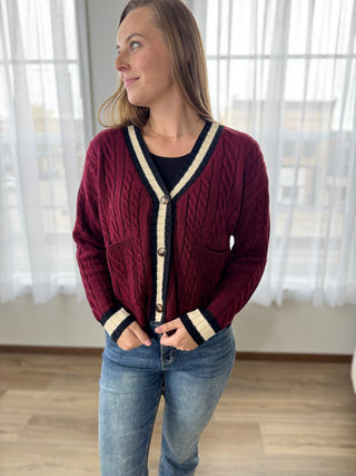 Woman wearing a burgundy cable knit cardigan with white trim indoors.