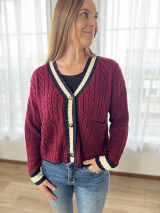 Woman wearing a red cable knit cardigan with white trim indoors.