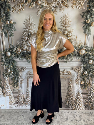Woman in a silver top and black skirt standing in front of a decorated Christmas fireplace.