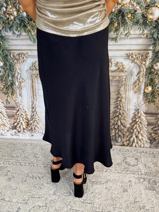 Person wearing a black skirt and gold top in front of decorative Christmas trees.