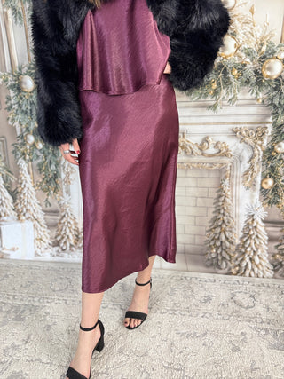 Person wearing a burgundy outfit with a fur coat in a decorated room.