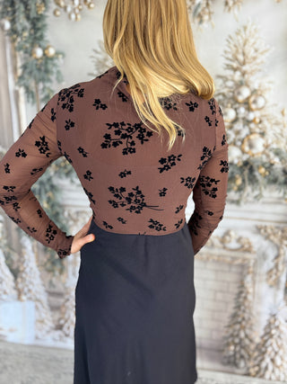 Person wearing a brown floral top with a blurred decorative background