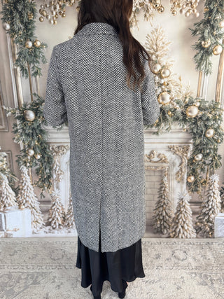 Person wearing a long, patterned coat in a decorated room with Christmas trees and lights.