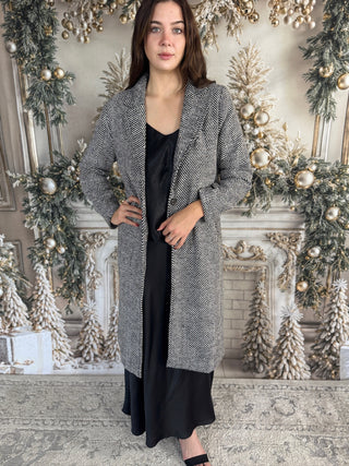 Woman wearing a long gray coat in a decorated room with Christmas trees and ornaments.