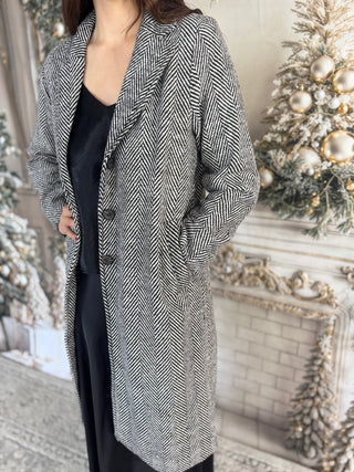 Person wearing a long, patterned coat in a festive indoor setting with Christmas decorations.