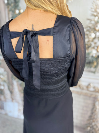 Black dress with open back and puffed sleeves worn by a person, blurred background