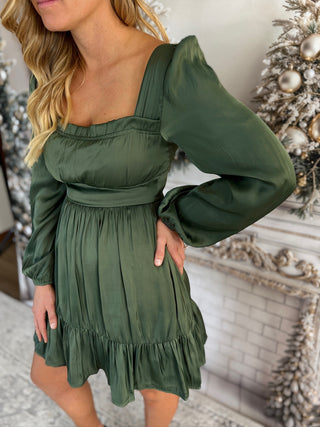 Woman wearing a green dress with long sleeves in a decorated room.