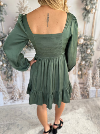 Green dress with long sleeves and ruffled hem worn by a person, with a decorative background.