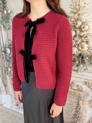 Person wearing a red textured jacket with black bow details against a decorative background
