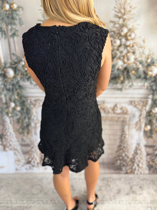 Person wearing a black lace dress in a decorated room with Christmas trees.