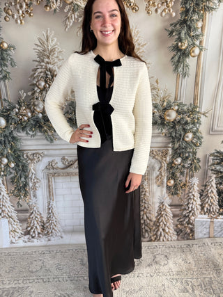 Woman in a white blazer and black dress standing in a decorated room with Christmas trees.