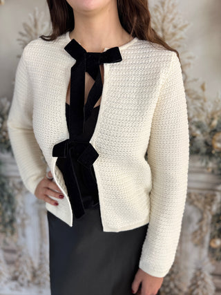 White textured blazer with black ribbon details worn by a person against a neutral background
