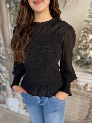 Woman wearing a black smocked top and blue jeans with a decorative background