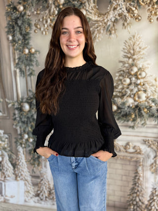 Woman wearing a black blouse with ruffled details in front of a decorated Christmas background