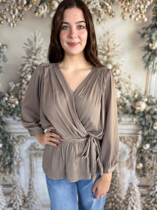 Woman wearing a taupe wrap top with a blurred decorative background