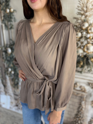 Woman wearing a taupe wrap top with long sleeves in front of a decorated Christmas tree.