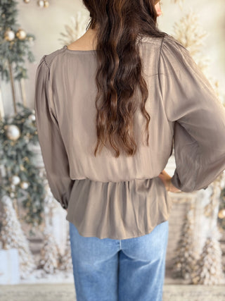 Person wearing a beige blouse with long sleeves and blue jeans, standing in front of a decorated Christmas tree.