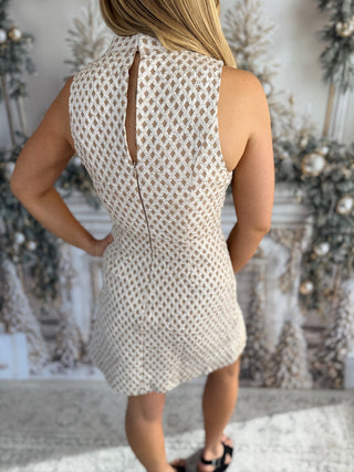 Woman wearing a beige sleeveless dress with a textured pattern against a decorative background.