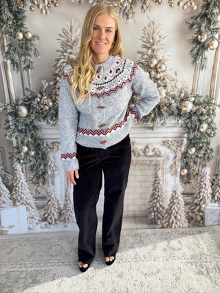 Woman wearing a patterned sweater and black pants in a decorated room with Christmas trees.