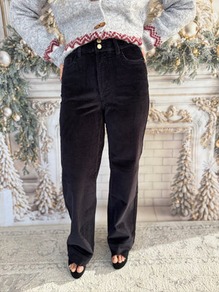 Person wearing a gray sweater with red trim and black pants in front of a decorated Christmas fireplace.