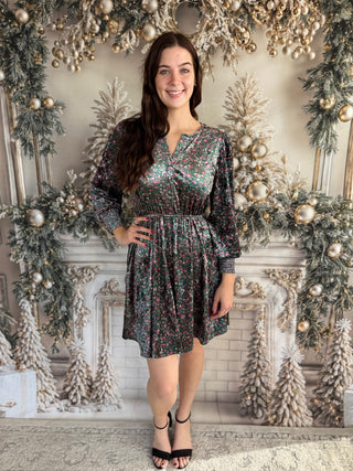 Woman in a floral dress standing in front of a decorated fireplace with Christmas trees.