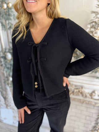 Woman wearing a black outfit with a textured cardigan in front of a decorative mirror.