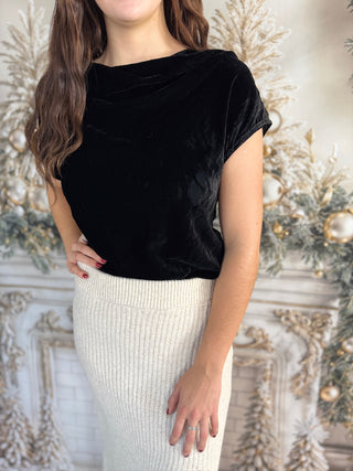 Person wearing a black velvet top and white skirt against a decorative background
