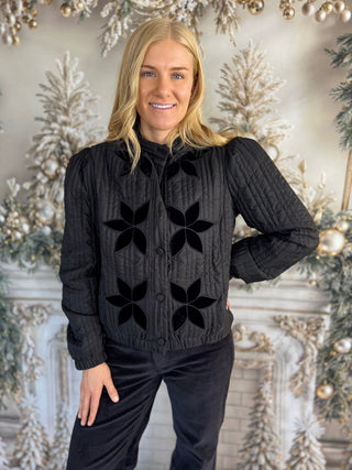 Woman wearing a black knit cardigan with star patterns in a decorated room.