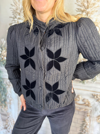 Person wearing a gray sweater with black floral patterns against a neutral background