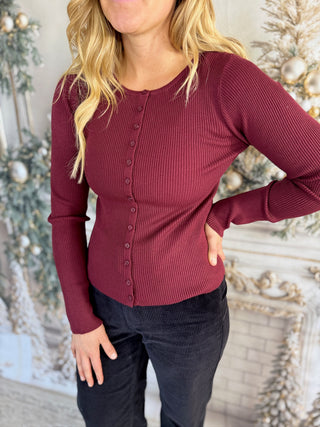 Person wearing a burgundy long-sleeve top with a Christmas tree in the background