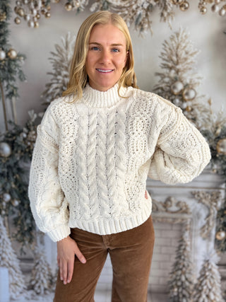 Woman wearing a cream cable knit sweater with a decorative background