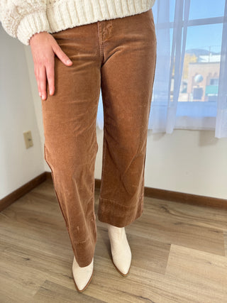 Person wearing brown corduroy pants and white shoes indoors.
