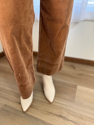 Brown corduroy pants with white pointed-toe boots on a wooden floor.