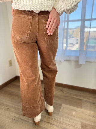 Person wearing brown corduroy pants in a room with a window in the background
