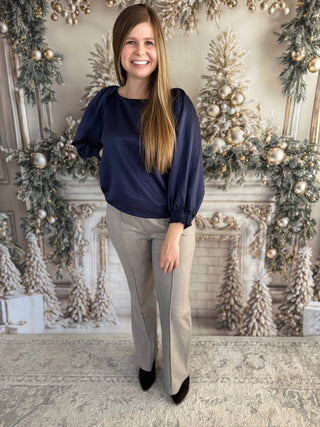 Woman in a blue blouse and beige pants standing in front of a decorated fireplace.