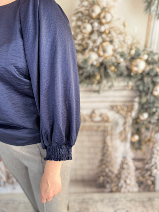 Person wearing a navy blue long-sleeve top with a blurred decorative background