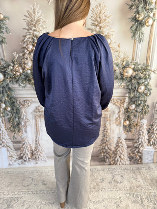 Person wearing a navy blue blouse with puffed sleeves in a decorated room.