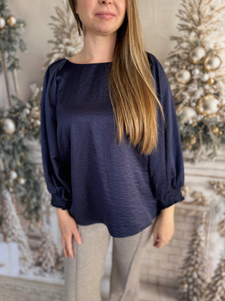 Woman wearing a navy blue blouse with balloon sleeves in a decorated room.