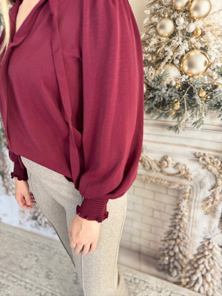 Person wearing a burgundy blouse with a decorative Christmas tree in the background