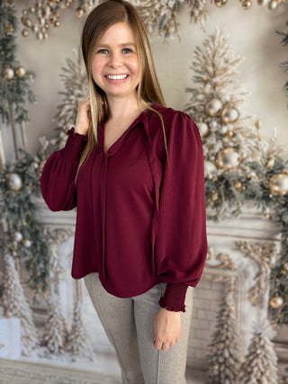 Woman wearing a burgundy blouse in front of a decorated Christmas tree.
