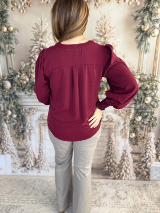 Person wearing a burgundy top and gray pants in a decorated room with Christmas trees.