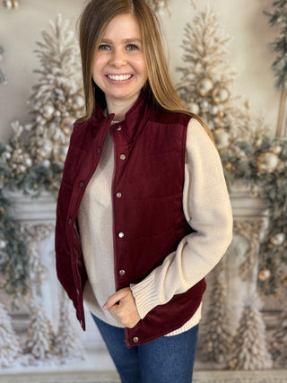 Woman wearing a red vest over a cream sweater with a decorated background