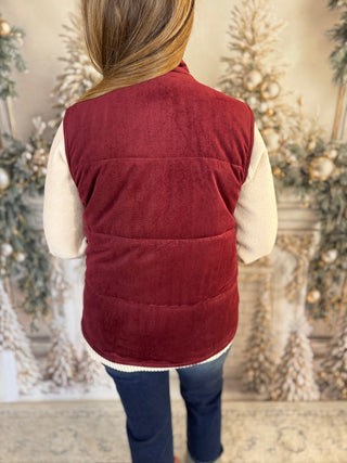 Person wearing a red puffer vest in front of decorated Christmas trees.